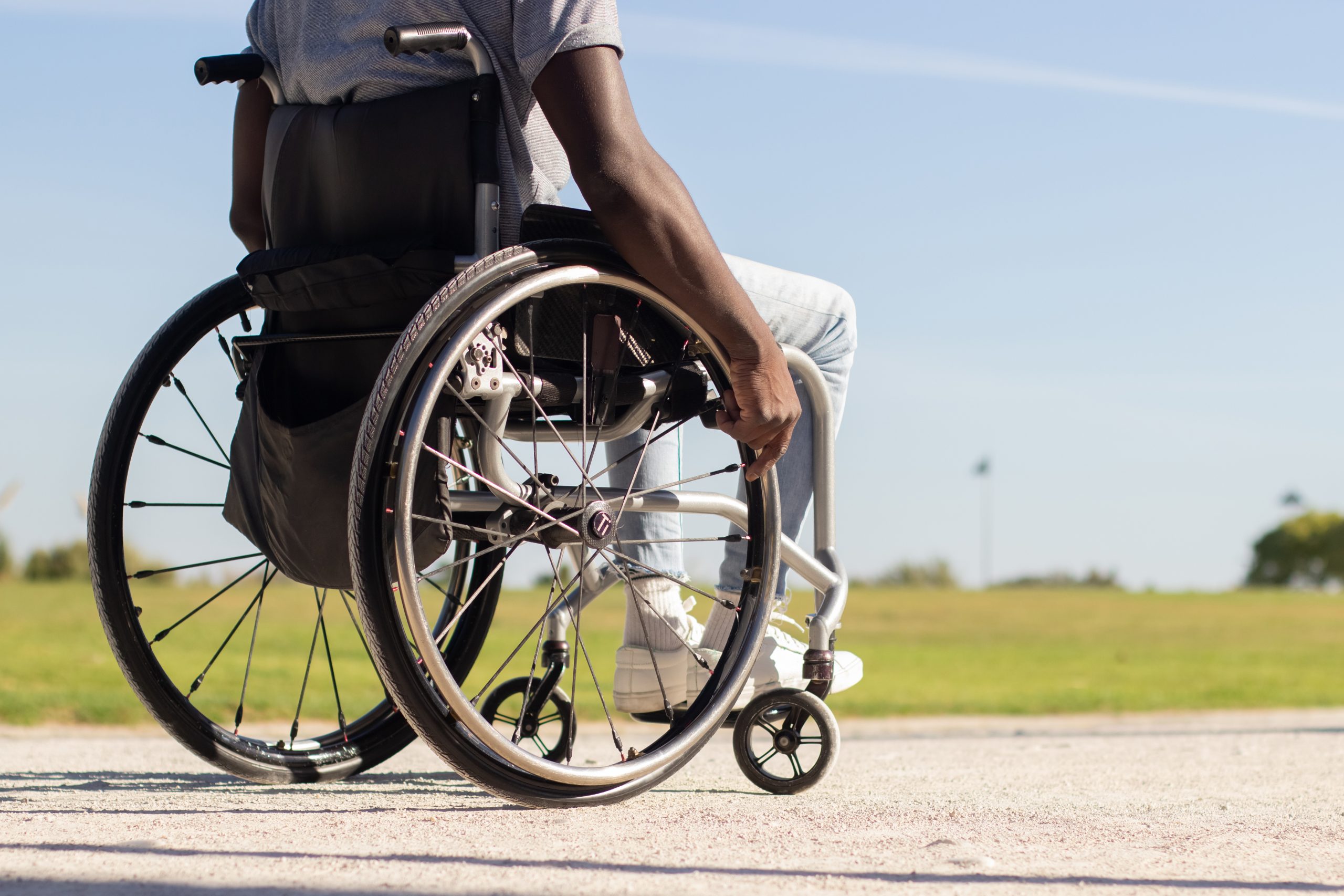 Black man in wheelchair riding along park road. African American guy with disability enjoying warm summer day outside. Closeup shot of wheels. Back view. Disability, lifestyle concept.